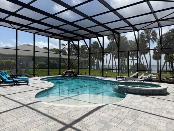 A pool area with a glass enclosure, lounge chairs, and a view of palm trees and a body of water.