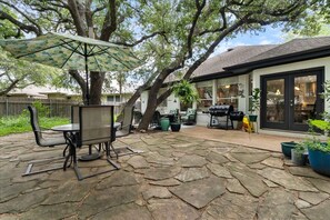 A patio with stone flooring, a table and chairs, a grill, and a large umbrella. - FULLY REMODELED-BEST LOCATION IN AUSTIN Pet Friendly-Gateway to the Hill Country (Austin)