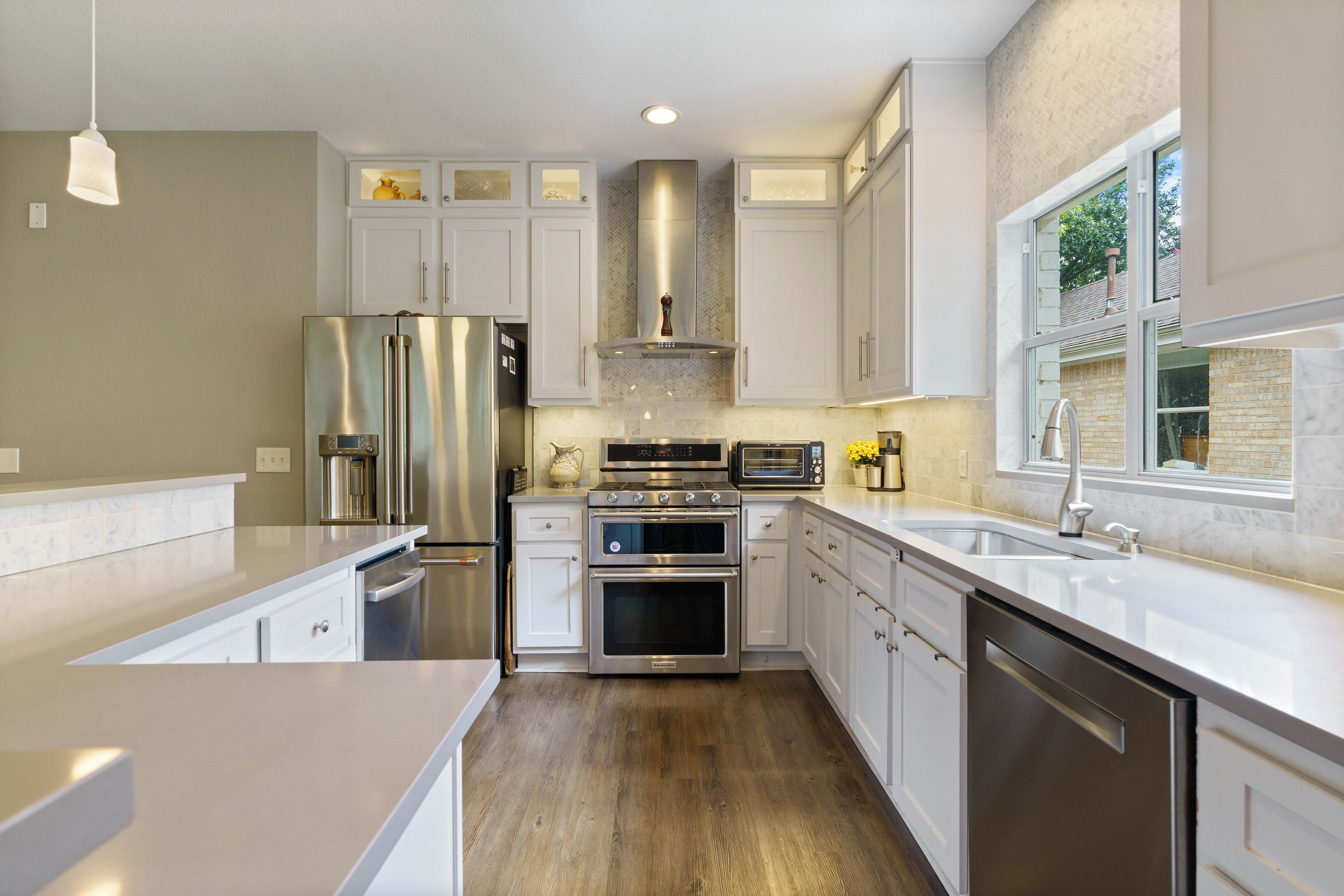 A modern kitchen with stainless steel appliances, white cabinetry, and a large window providing natural light.