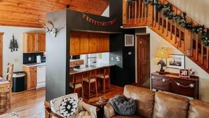 A cozy living room with a fireplace, a dining area, and a kitchen. - Little Creek Cabin (Branson West)