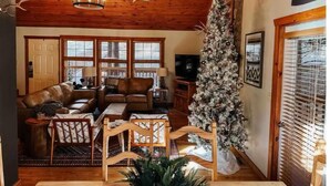 A cozy living room with a wooden ceiling, a large Christmas tree, leather sofas, and a chandelier. - Little Creek Cabin (Branson West)