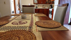 Comedor con una larga mesa de madera, individuales tejidos y una silla tapizada en gris.