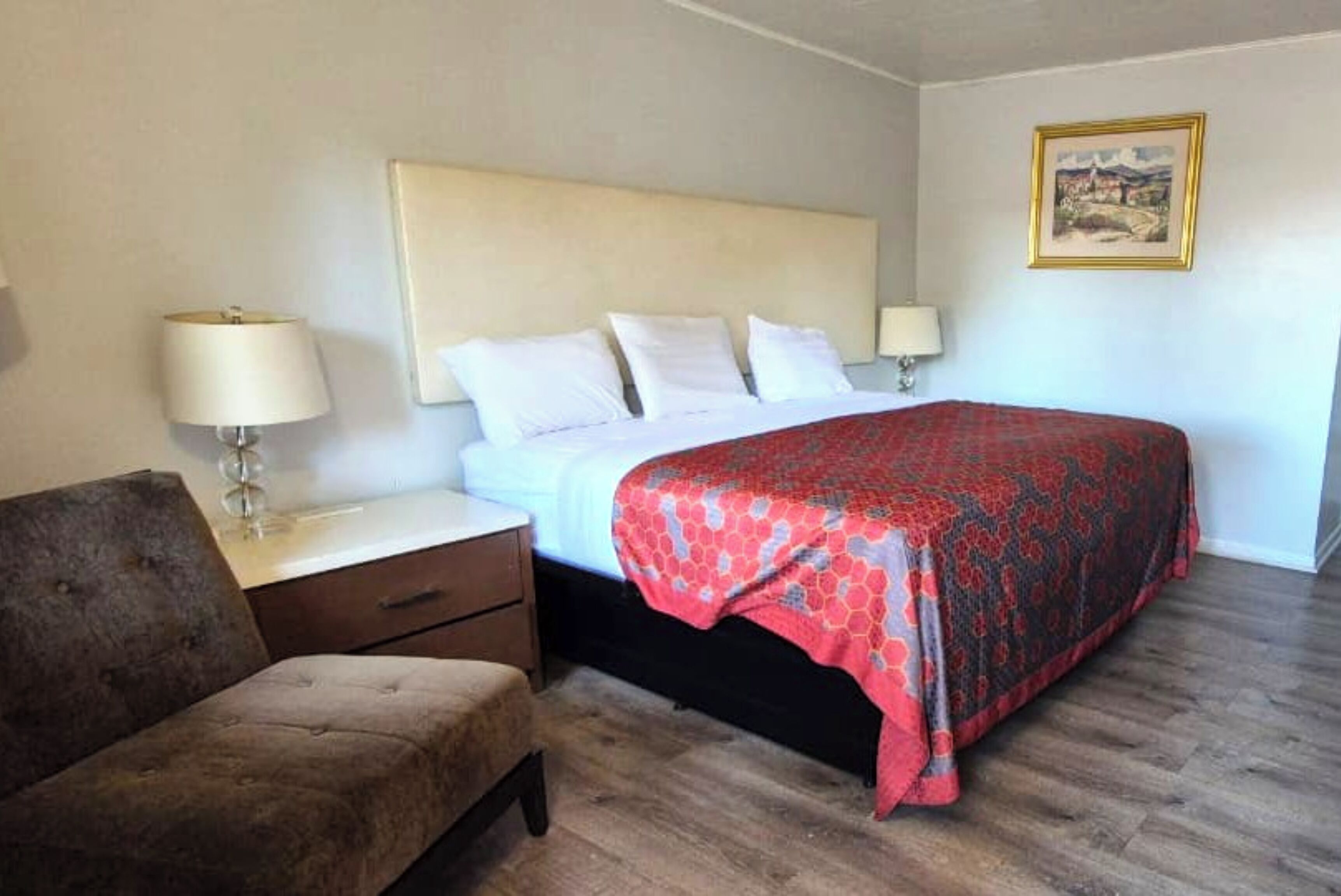 A bedroom with a bed, two bedside lamps, a nightstand, a chair, and a framed picture on the wall.