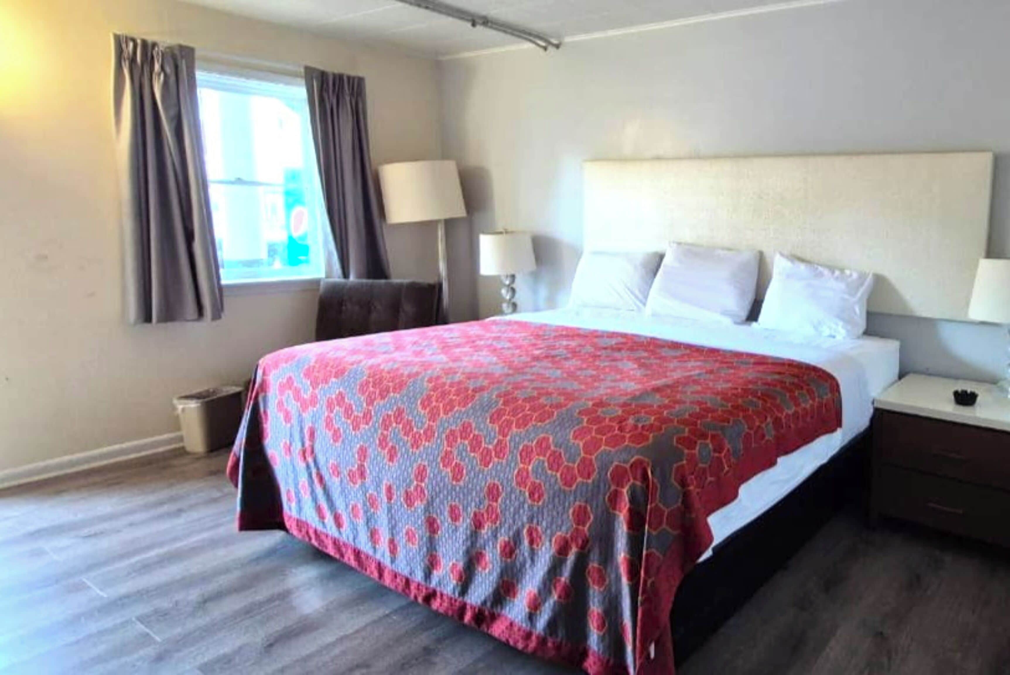 Ein Hotelzimmer mit einem großen Bett, zwei Nachttischlampen, einem Nachttisch und einem Fenster mit Vorhängen.