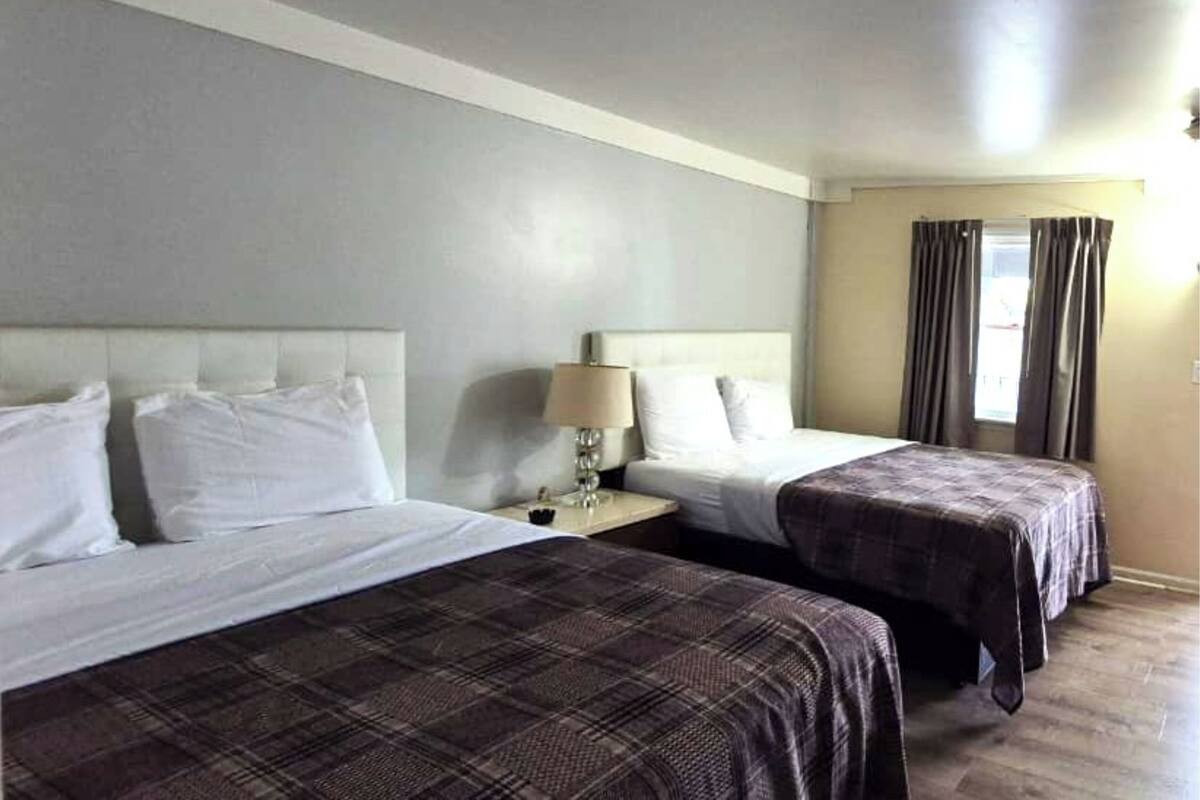 A hotel room with two beds, a nightstand with a lamp, and a window with curtains.