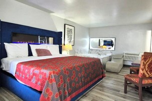 Quarto de hotel com uma cama grande, uma escrivaninha, uma cadeira, um espelho e banheiro com banheira e chuveiro.