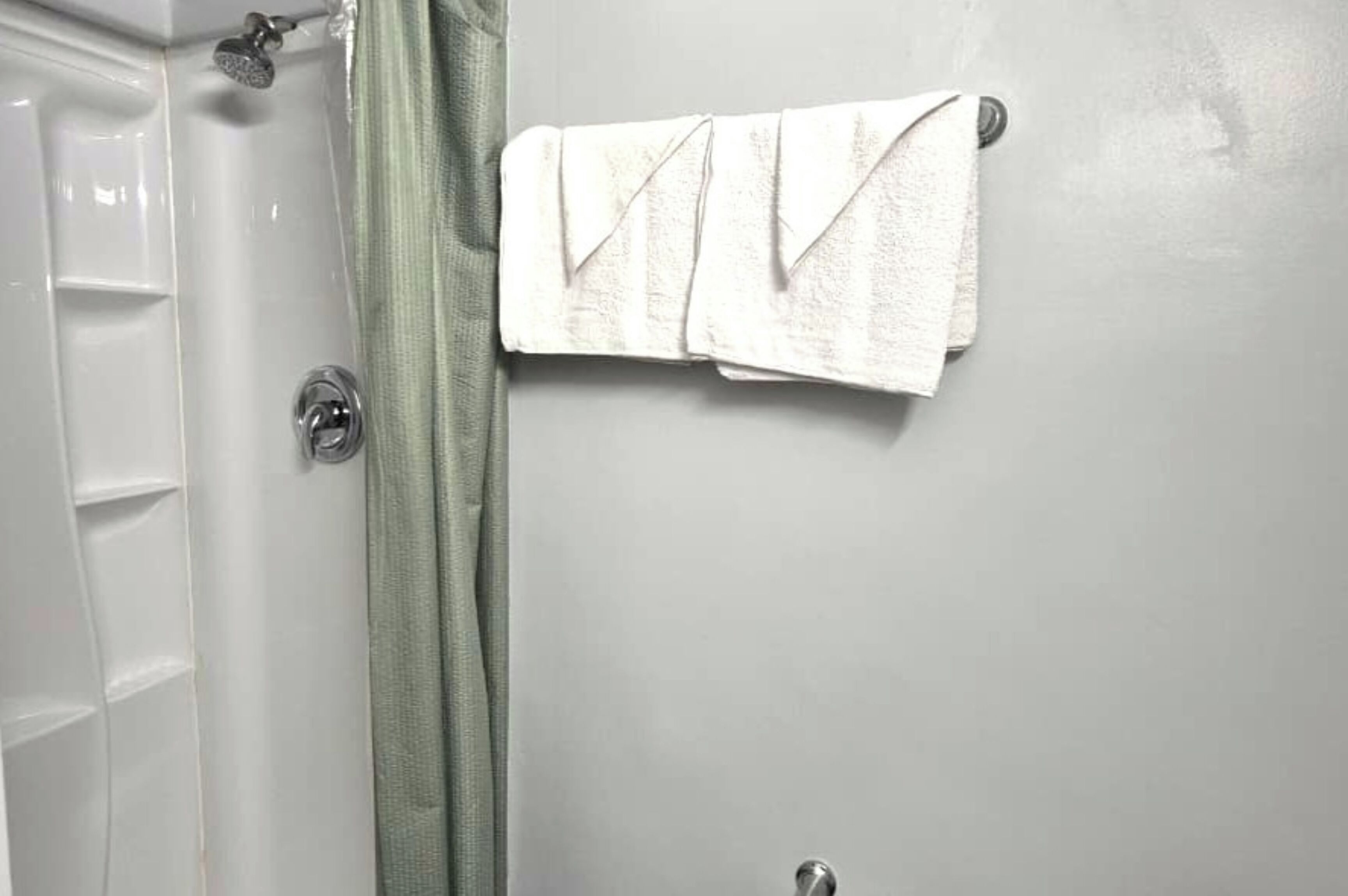 A bathroom with a white door, a shower, and a towel rack with two towels.