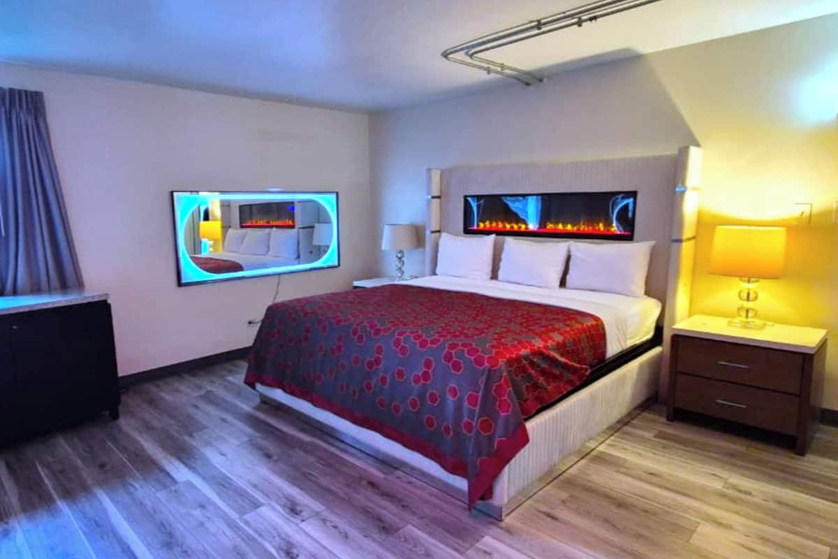 A modern hotel room with a bed, bedside tables, a TV, and a fireplace.