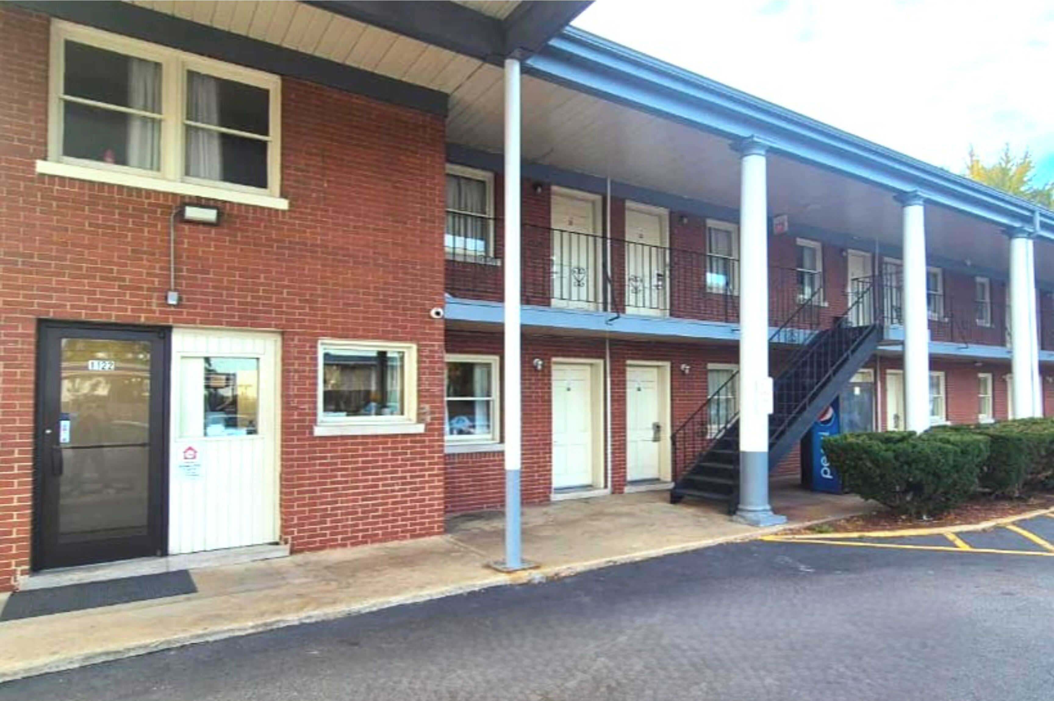 A multi-story brick building with a covered entrance, a Pepsi vending machine, and a parking area.