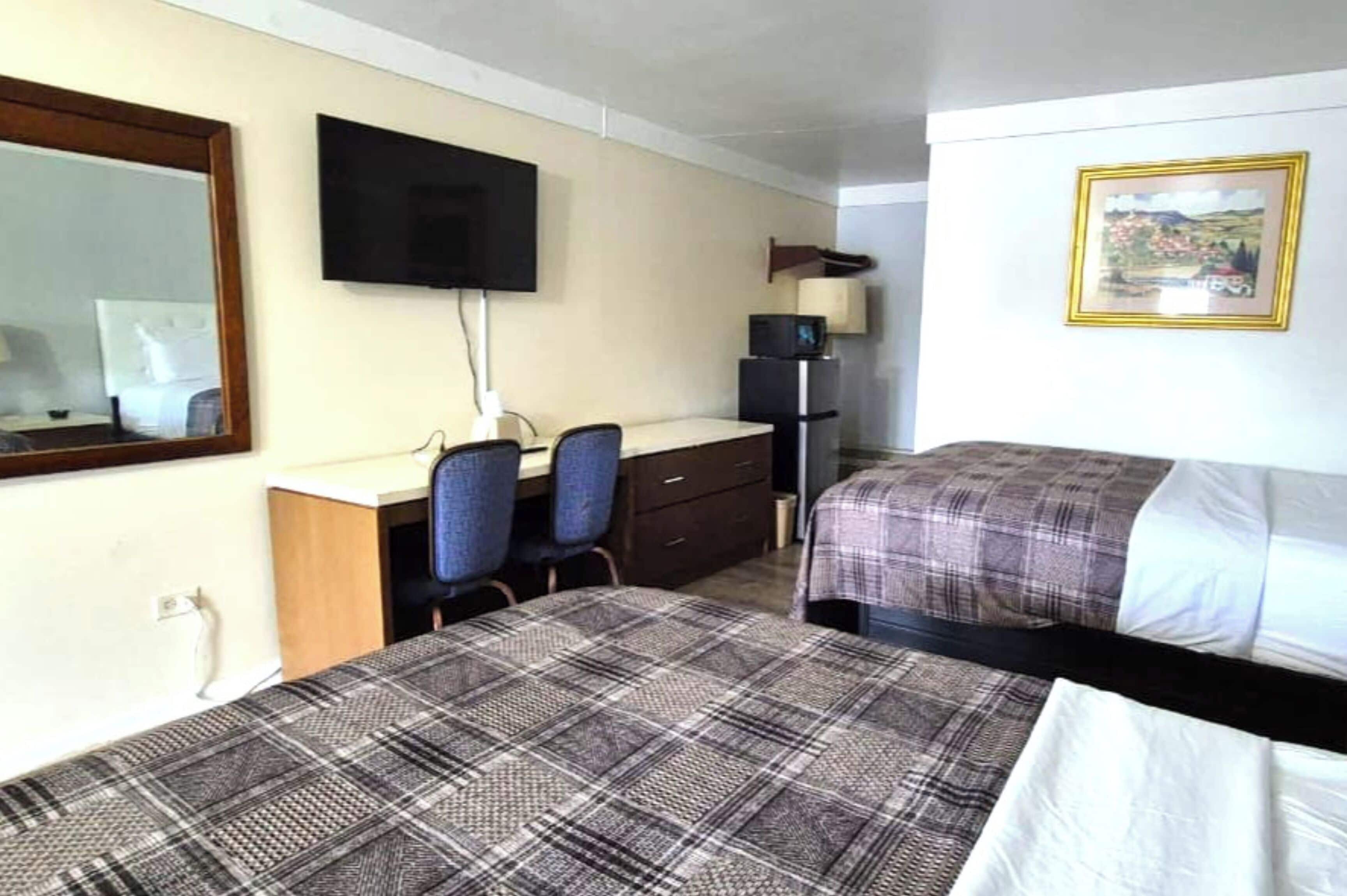 A hotel room with two beds, a desk with a chair, a television, and a framed picture on the wall.