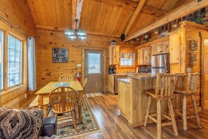 A wooden cabin interior with a dining area, kitchen, and bar seating.