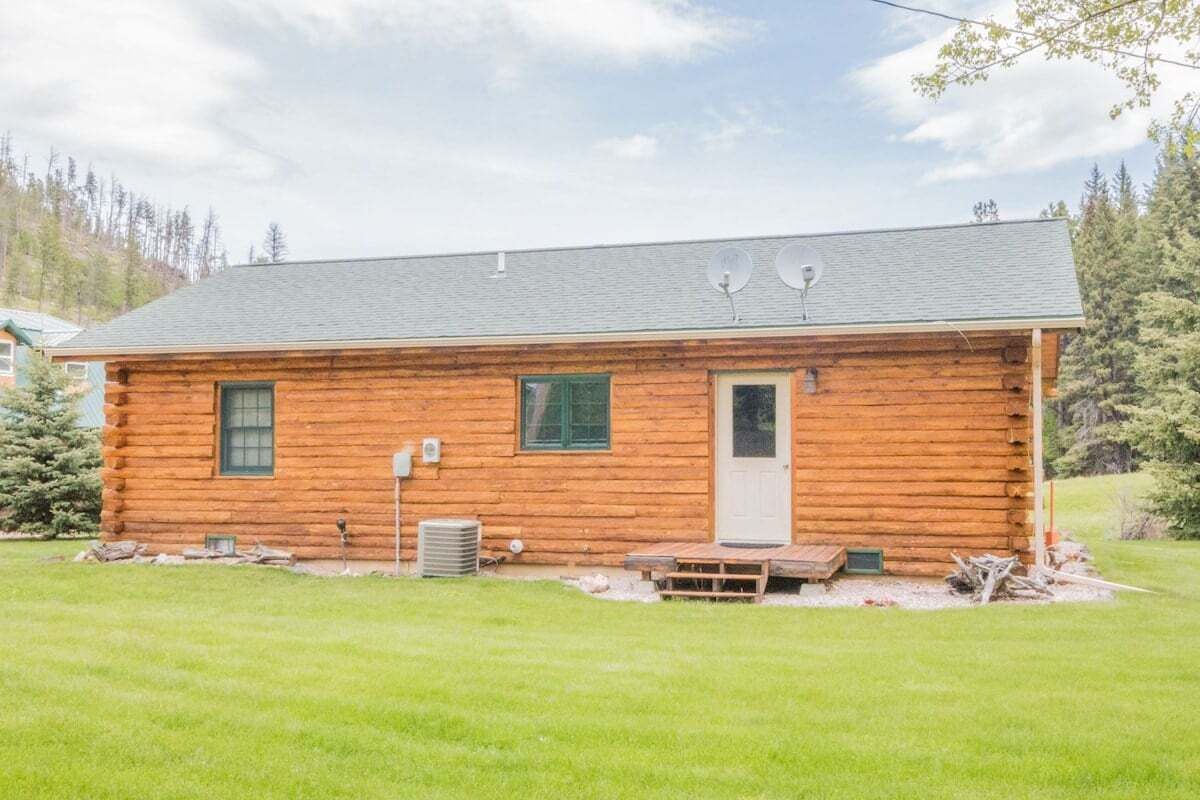 Une cabane en rondins avec une porte d’entrée, deux fenêtres et un petit porche.