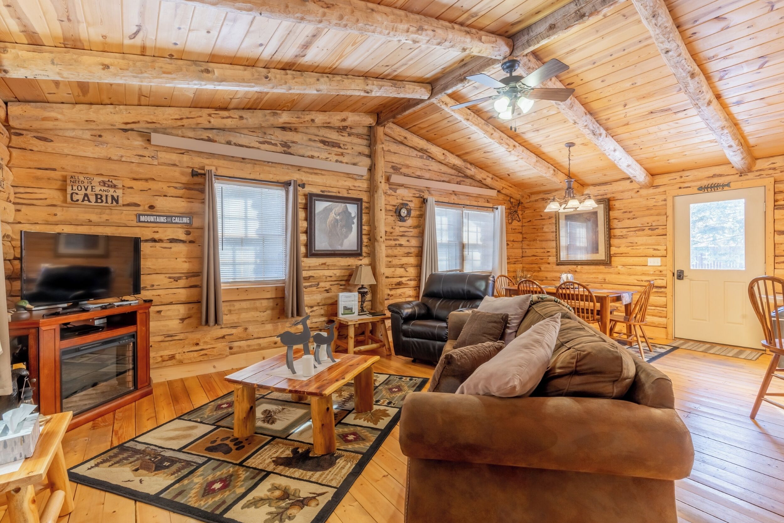 A log cabin interior with a television, leather chair, wooden table, and a fireplace.