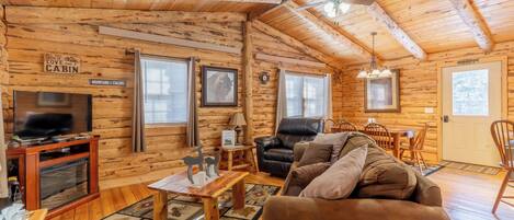 A log cabin interior with a television, leather chair, wooden table, and a fireplace.