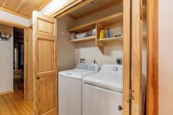 Une buanderie avec deux machines à laver blanches, des étagères en bois au-dessus et une porte en bois.