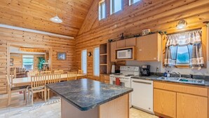 L’intérieur d’une cabane en rondins comprend une cuisine, un coin repas et une grande fenêtre.