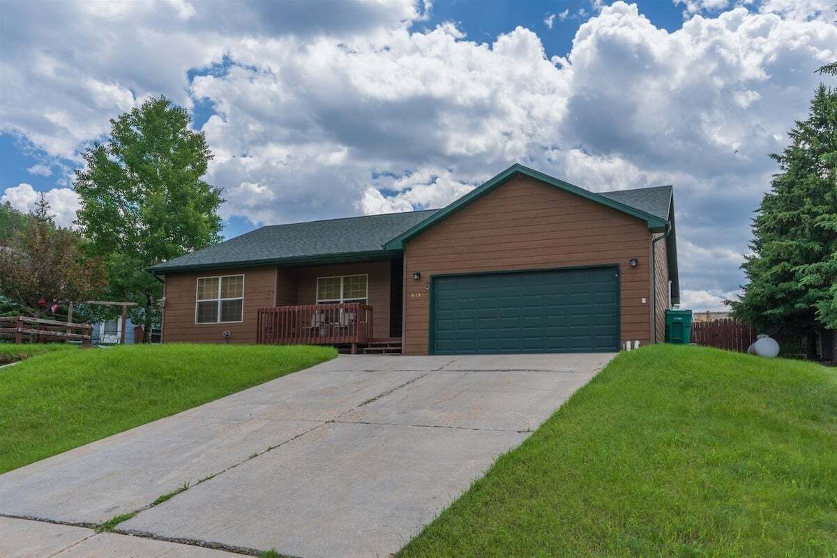 Une maison de plain-pied avec un garage vert, un porche à l’avant et une pelouse bien entretenue.