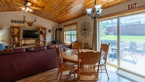 Un interior de madera con un sofá de cuero, una mesa de comedor de madera y sillas, un ventilador de techo y un ventanal con vistas al exterior.