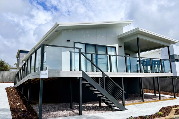 A modern house with a covered outdoor area, a staircase, and a view of the sky.