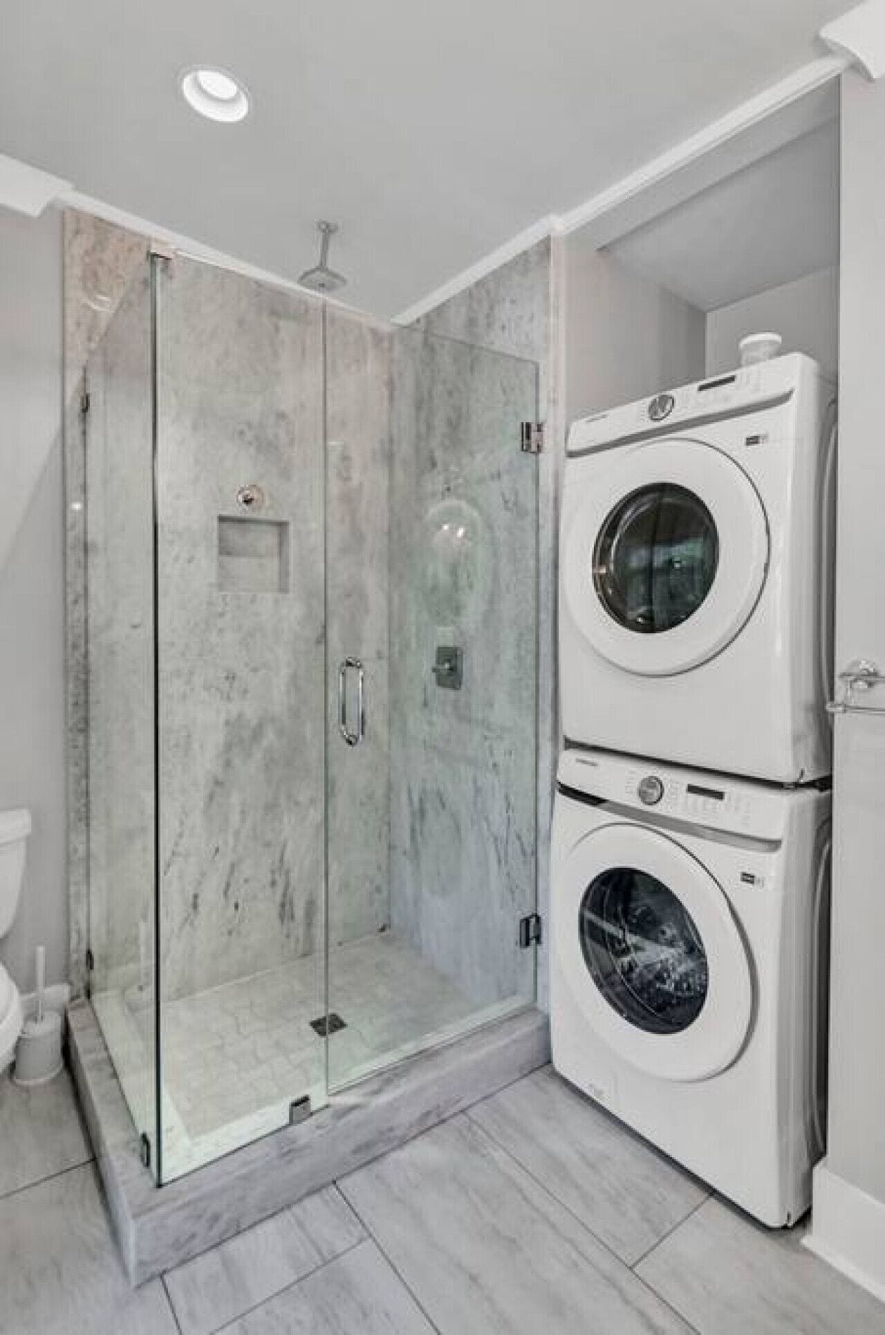 Une salle de bain avec une douche à parois de verre, des toilettes et un lave-linge et un sèche-linge superposés.