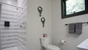Un baño con ducha, inodoro y ventana con vista a árboles.