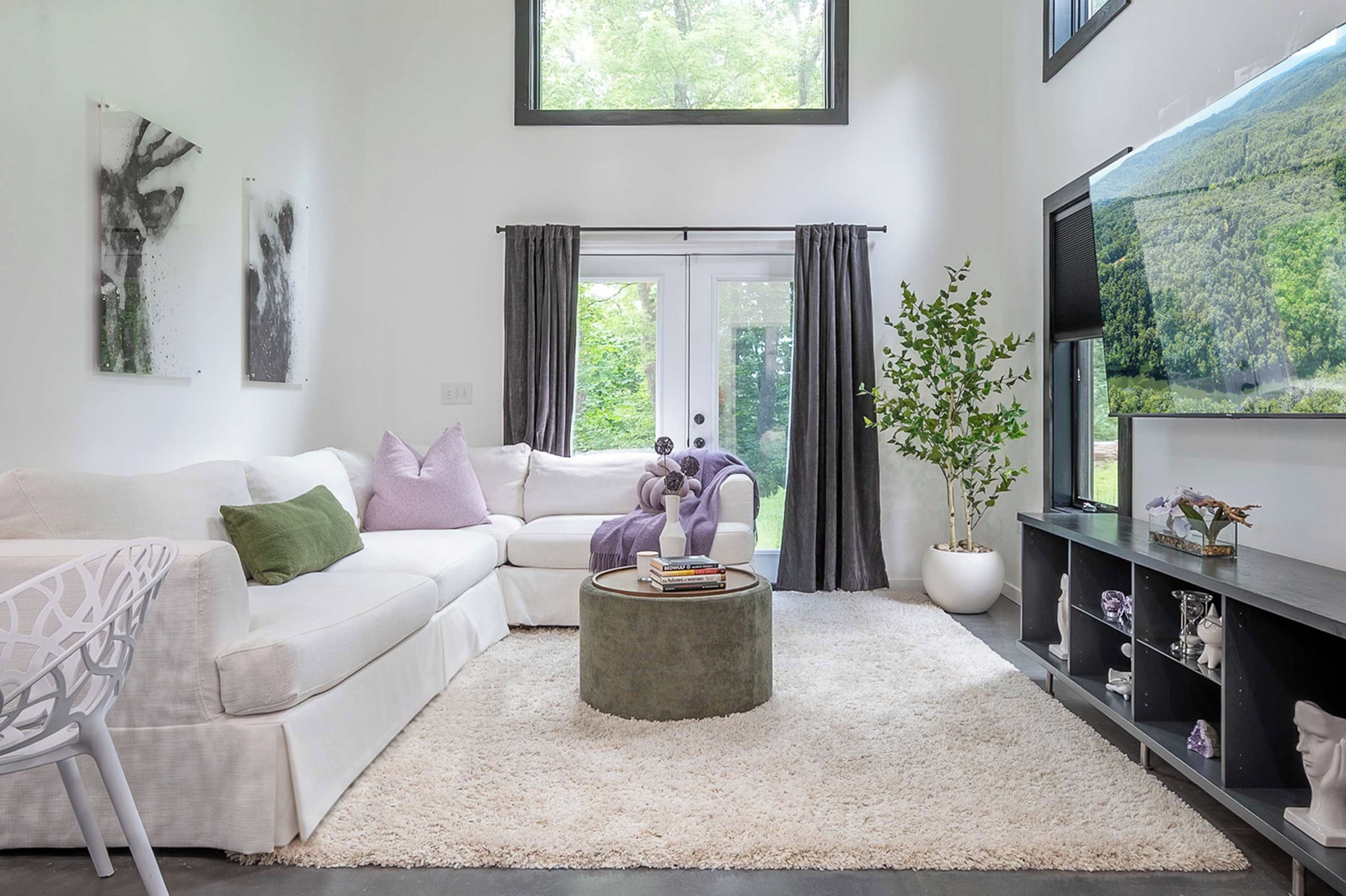 A modern living room with a white sofa, a coffee table, a TV, and a large window with curtains.
