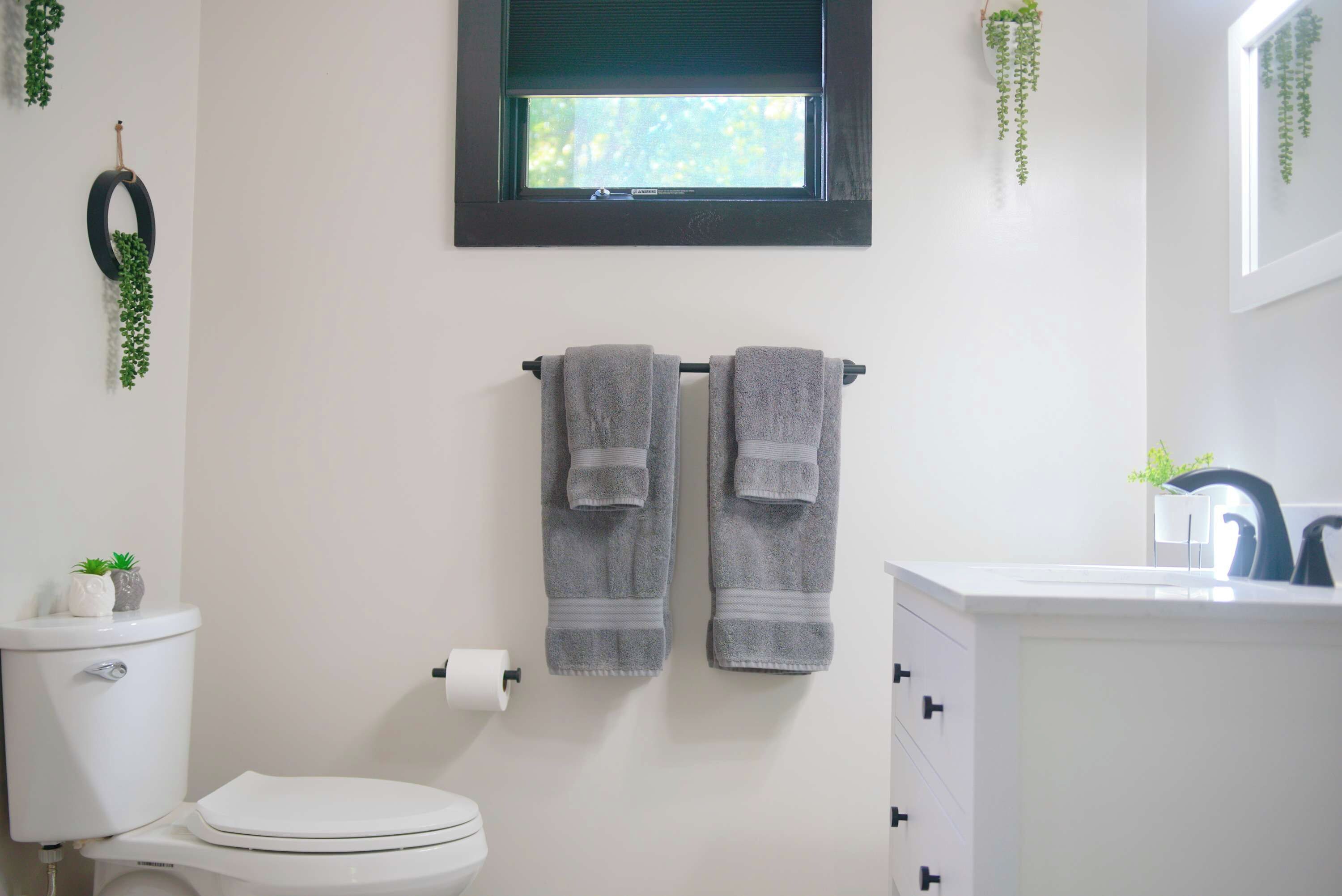 Een badkamer met toilet, een handdoekrek met twee handdoeken, een toiletpapierrol en een raam met uitzicht op groen.