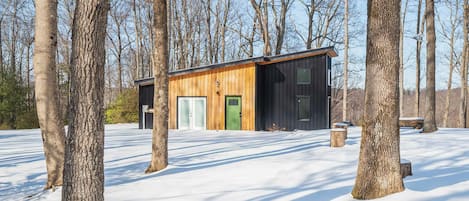 A cabin with a wooden exterior and a black door, surrounded by snow and trees.