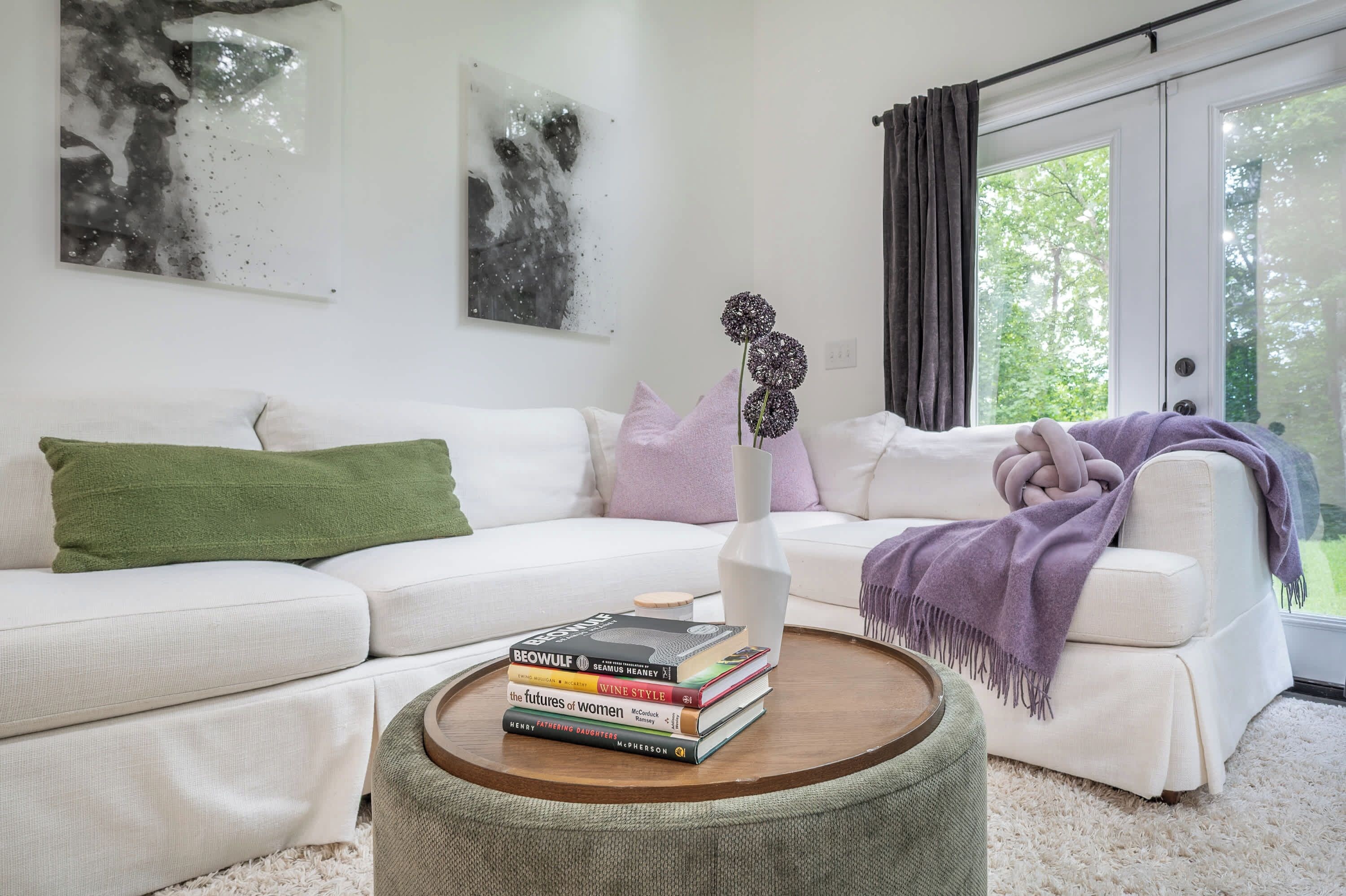 Una sala de estar con un sofá blanco, una mesa de centro redonda de madera y un jarrón con flores.