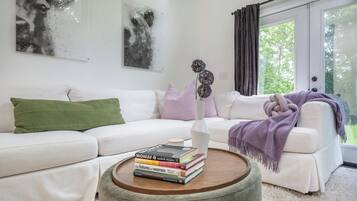 Una sala de estar con un sofá blanco, una mesa de centro redonda de madera y un jarrón con flores.