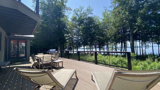 Une terrasse dotée de mobilier d’extérieur, d’un barbecue et offrant une vue sur un lac entouré d’arbres.