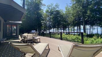 A deck with outdoor furniture, a grill, and a view of a lake surrounded by trees.