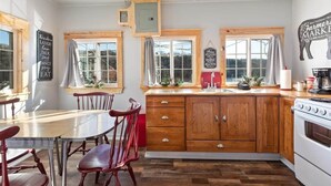 A kitchen with wooden cabinets, a stove, and a dining table with chairs. - Historic Rockaway Beach Cottage 8 (Rockaway Beach)