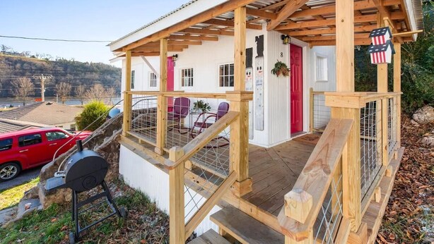 A wooden deck with a grill, a red car, and a white building with a red door. - Historic Rockaway Beach Cottage 8 (Rockaway Beach)