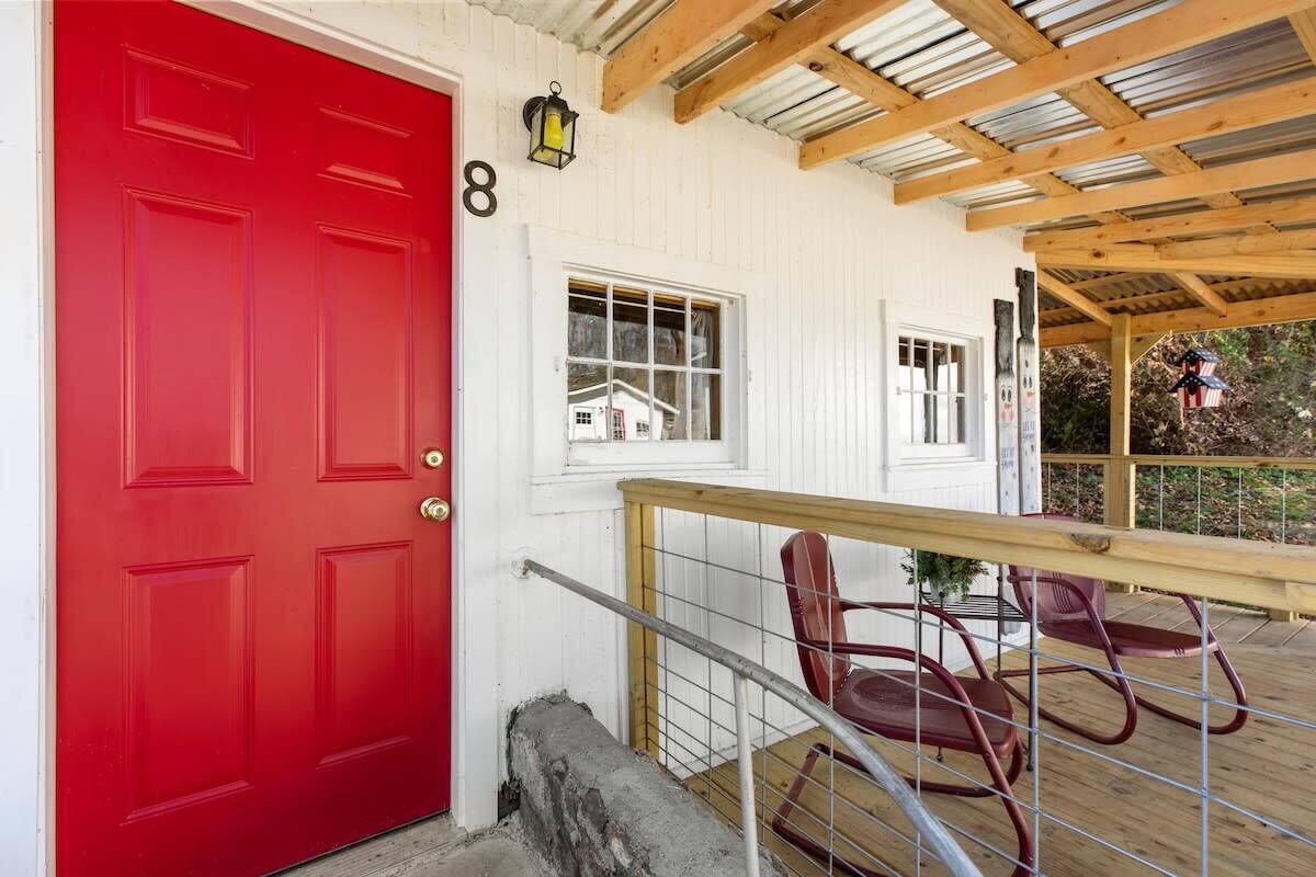A red door with a number '8' above it, a wooden deck with a railing, and two rocking chairs.