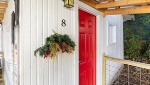 A white building with a red door, number 8, and a hanging wreath. - Historic Rockaway Beach Cottage 8 (Rockaway Beach)