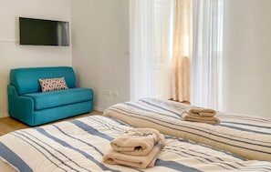 Una habitación con dos camas, un sofá azul, un televisor y cortinas translúcidas.