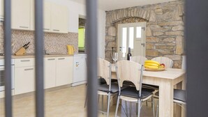 Une cuisine moderne avec des meubles blancs, un mur en pierre et un coin repas comprenant une table et des chaises en bois.