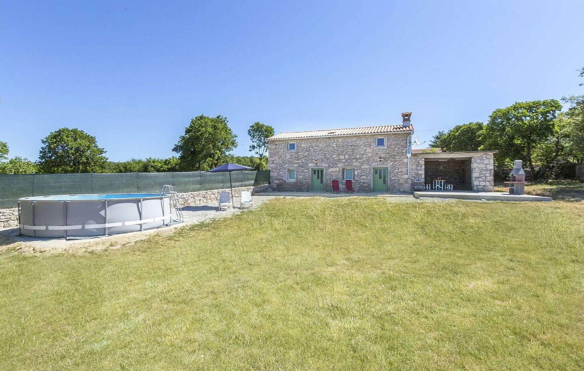 A stone house with a swimming pool, a small covered area, and a grassy yard.