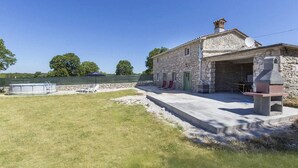 Une maison en pierre avec une piscine, un espace salon extérieur et un coin barbecue.