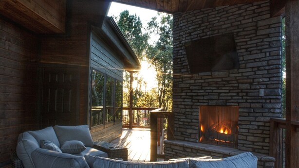 A cozy outdoor seating area with a stone fireplace, wicker furniture, and a view of the surrounding trees.