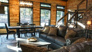A log cabin interior with a dining area, leather sofa, and a staircase.