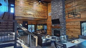 A spacious living area with a stone fireplace, a large TV mounted on the wall, and a cozy seating arrangement.