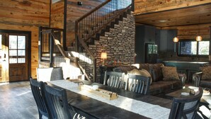A rustic interior with a stone staircase, wooden walls, a dining area with a long table, and a cozy seating area.