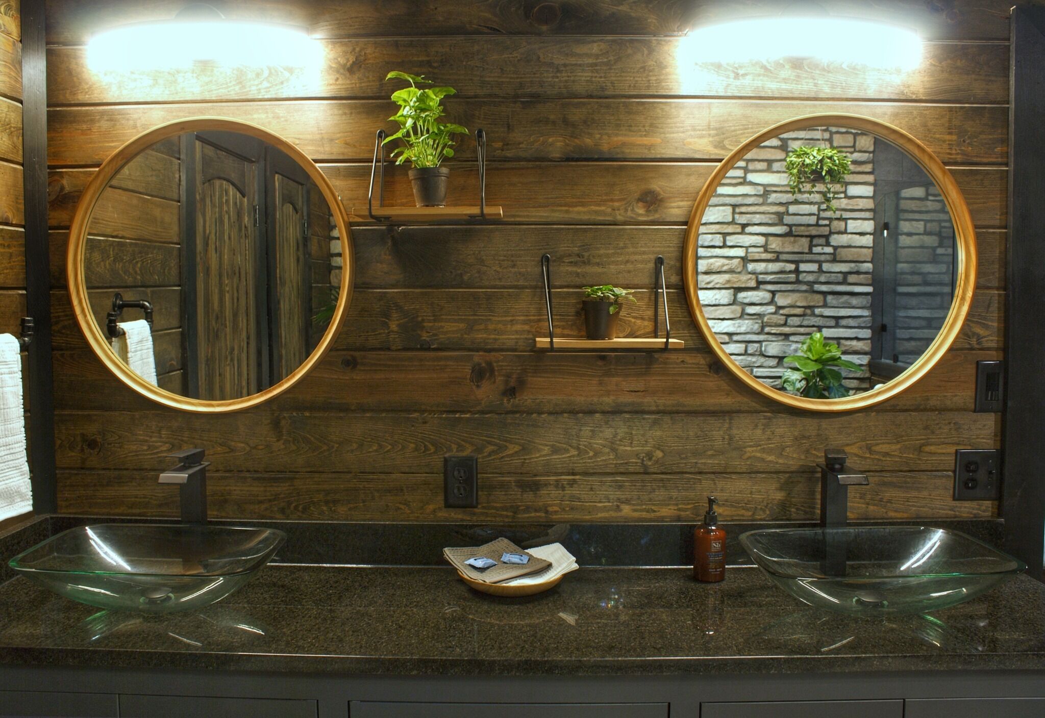 Un baño con paneles de madera, dos espejos redondos y dos lavamanos de vidrio.