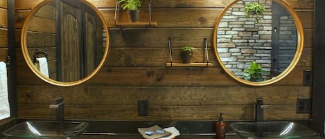 Un baño con paneles de madera, dos espejos redondos y dos lavamanos de vidrio.