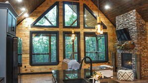 A cabin interior with a stone fireplace, wooden walls, and large windows.