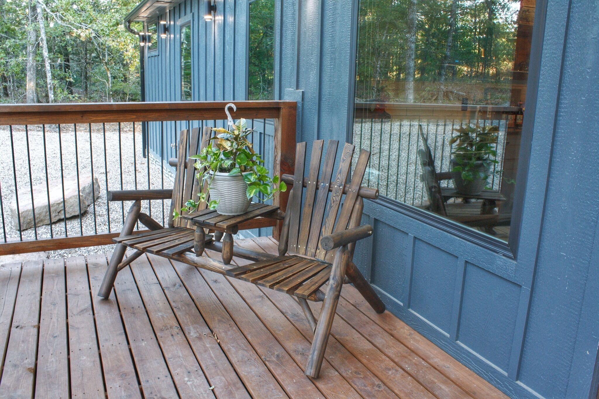 Terraza de madera con una silla y una mesa de madera, una planta colgante y una ventana con vistas a una zona de grava.