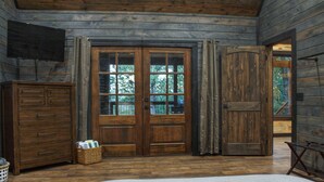 A rustic wooden room with a large bed, wooden wardrobe, and a set of double doors leading outside.
