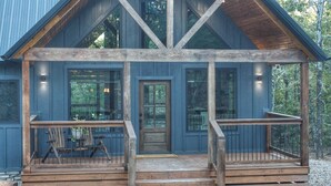 A rustic cabin with a wooden porch, large windows, and a door.